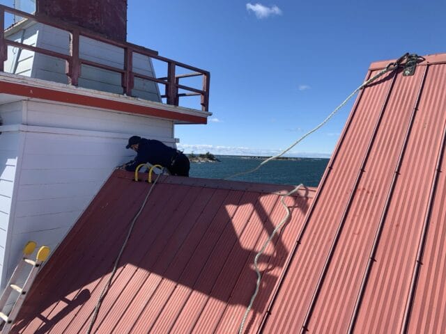 picture-1028385304 Gonneau Building Group field technician secured to a permanent roof harness point while working at height over the bay.