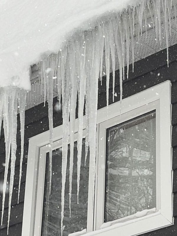 Ice dam ridge along the eaves of a cottage roof in Gravenhurst showing the buildup that forces meltwater back under the shingles and into the walls and ceilings below