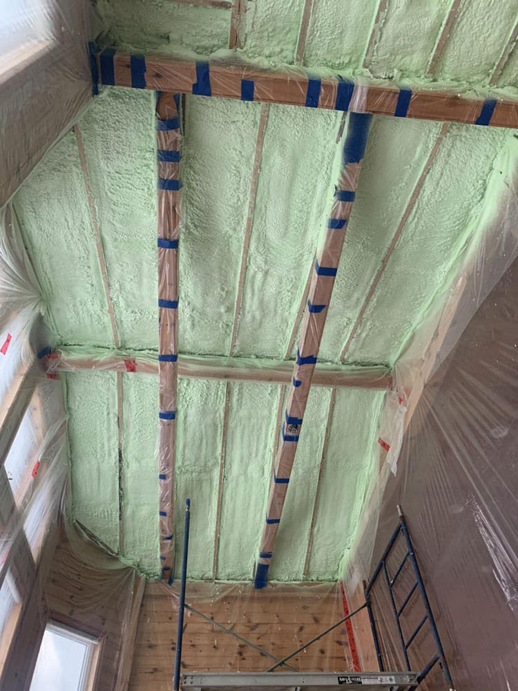 Closed-cell spray foam insulation in the rafter bays of a cathedral ceiling section of a Gravenhurst cottage, held clear of the roof deck so the ventilation channel above stays open, to permanently prevent ice dam formation