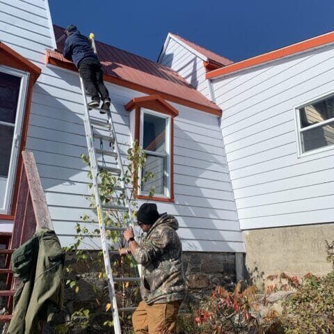 picture-1028436556 Proper ladder setup and footing while working above rock, vegetation, and changing shore conditions.